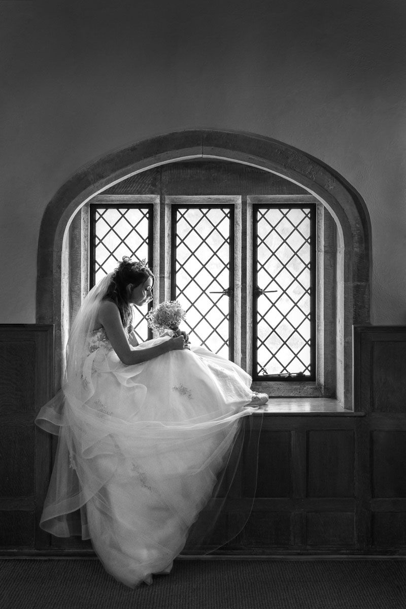 Bride in elegant pose sitting in window of Michelham Priory