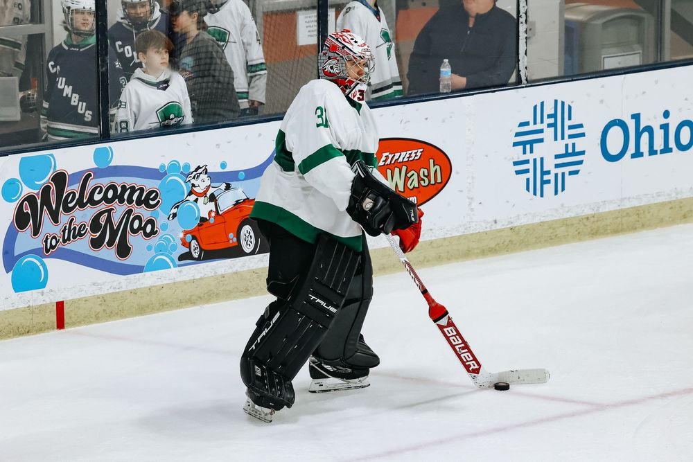 A hockey player in dark uniform handles the puck on ice with arena boards displaying Ohio signage in the background.