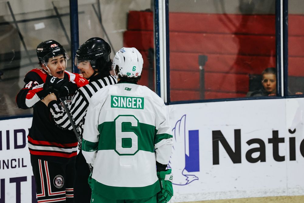 Hockey players from opposing teams battle for control of the puck along the boards during an intense game.