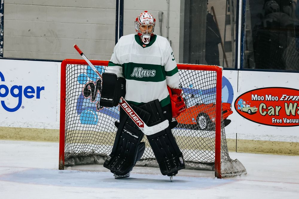 A hockey goalie in black and white uniform crouches in front of the net during a game.