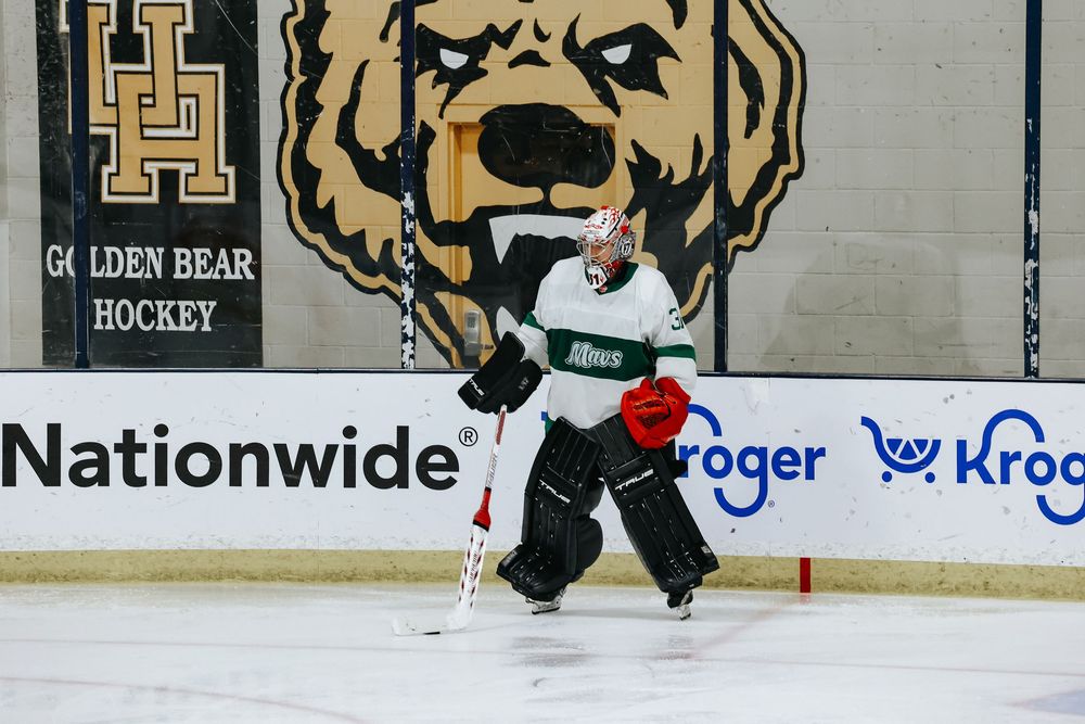 Hockey players battle for the puck during an intense game on the ice rink with advertisements visible in background.