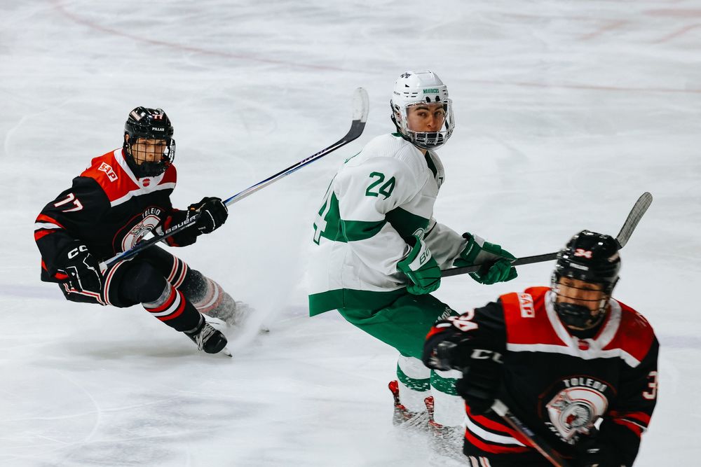 Hockey players in black and green jerseys battle for the puck during an intense game on the ice.