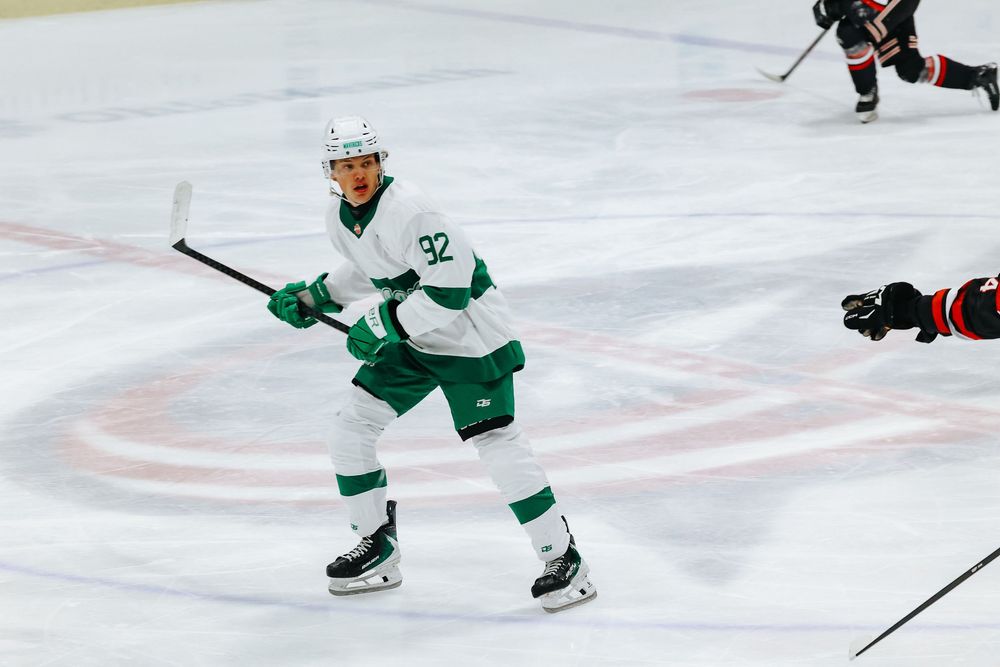 Hockey player in white and green uniform handles puck on ice during competitive game.