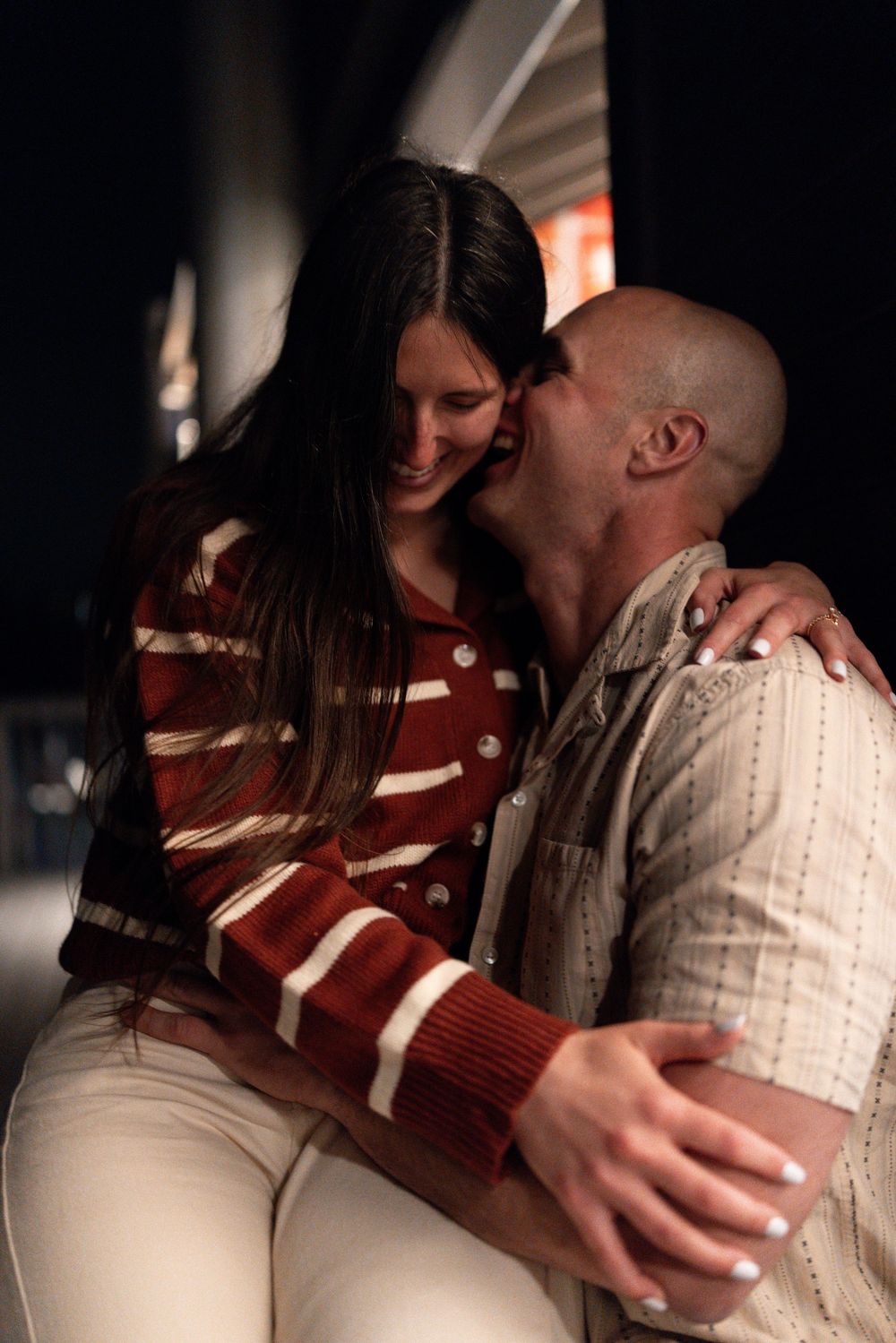 A couple in casual attire sharing an intimate embrace in a dimly lit setting.