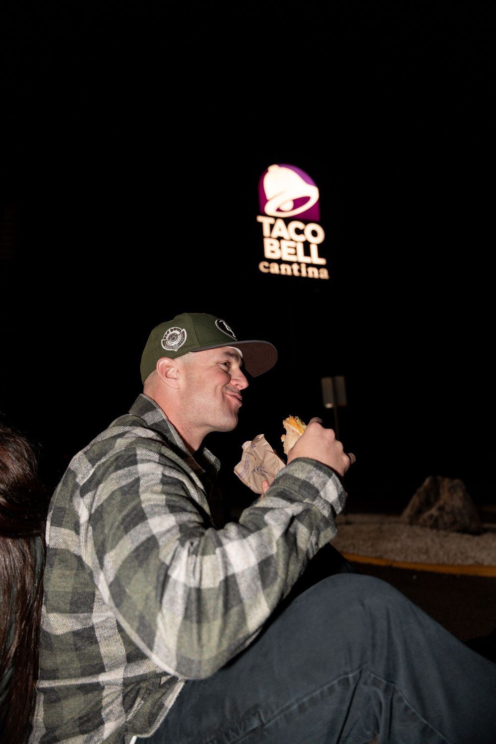 A performer in a plaid shirt and baseball cap sings passionately into a microphone during a nighttime show.