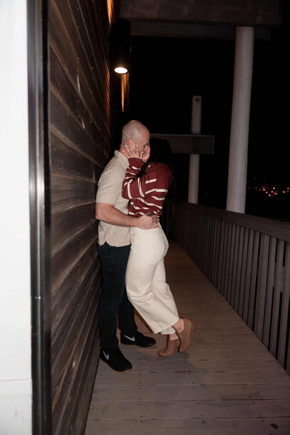 Two people share an intimate embrace on a dimly lit porch at night.