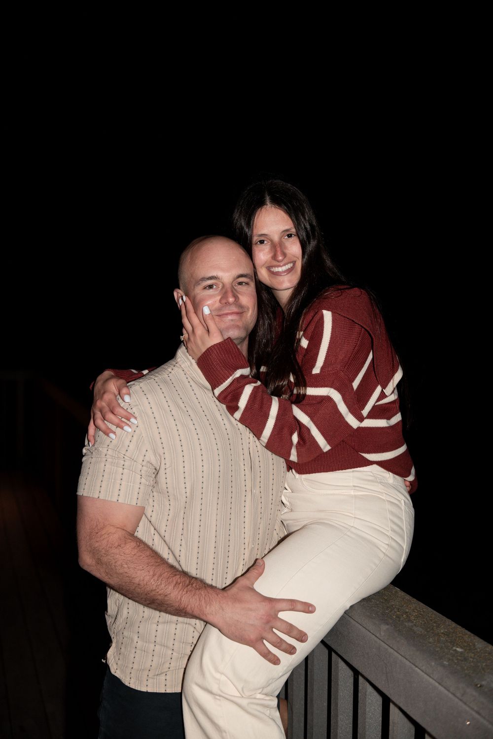 A couple hugs warmly while standing on a deck in dark evening lighting.