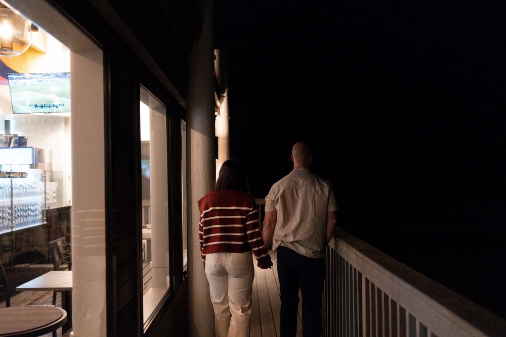Person standing on a dark porch at night with illuminated windows and railings visible in the background.