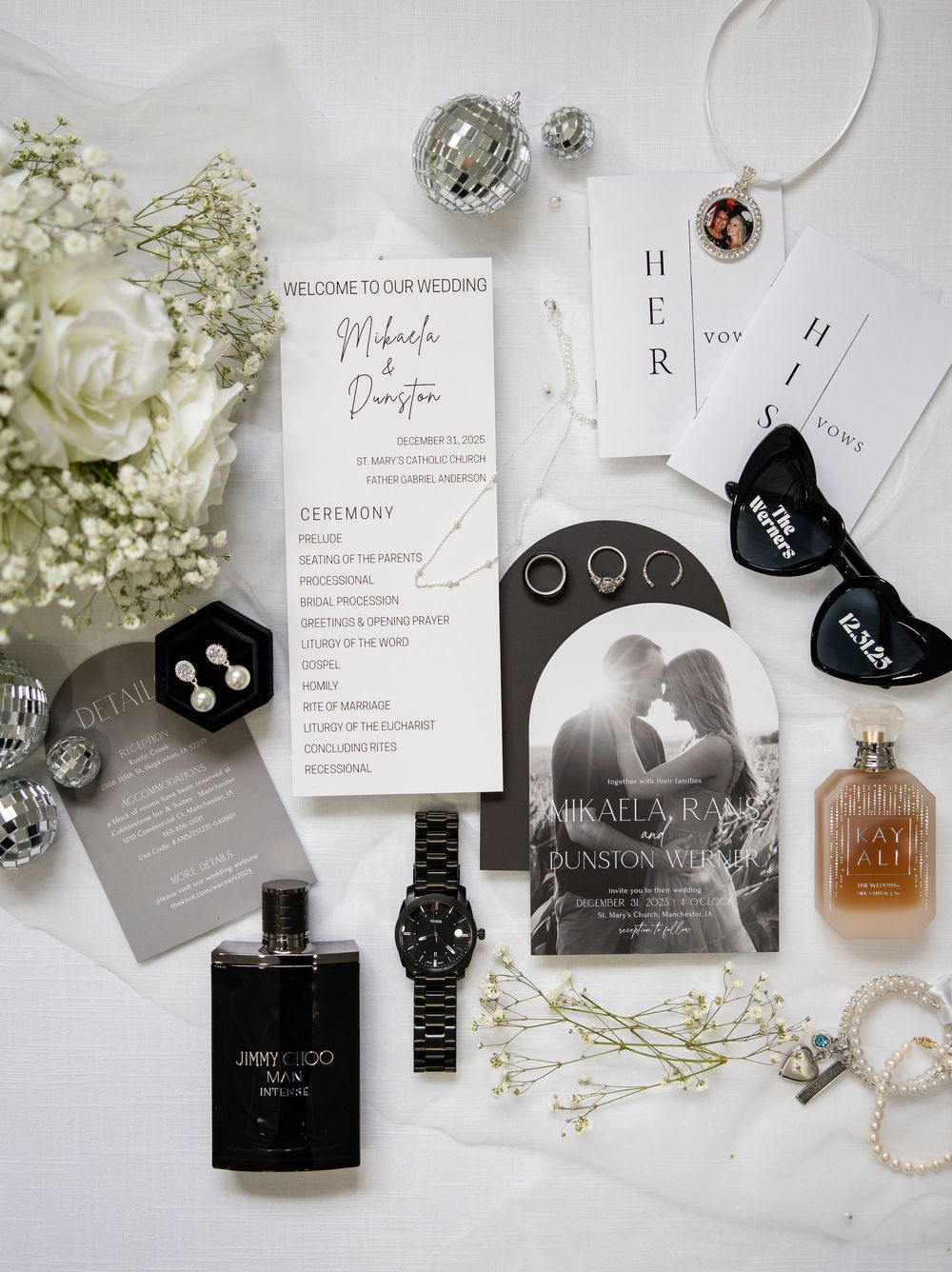 Wedding details flatlay with invitation, rings, perfume, watch and white flowers on light background.