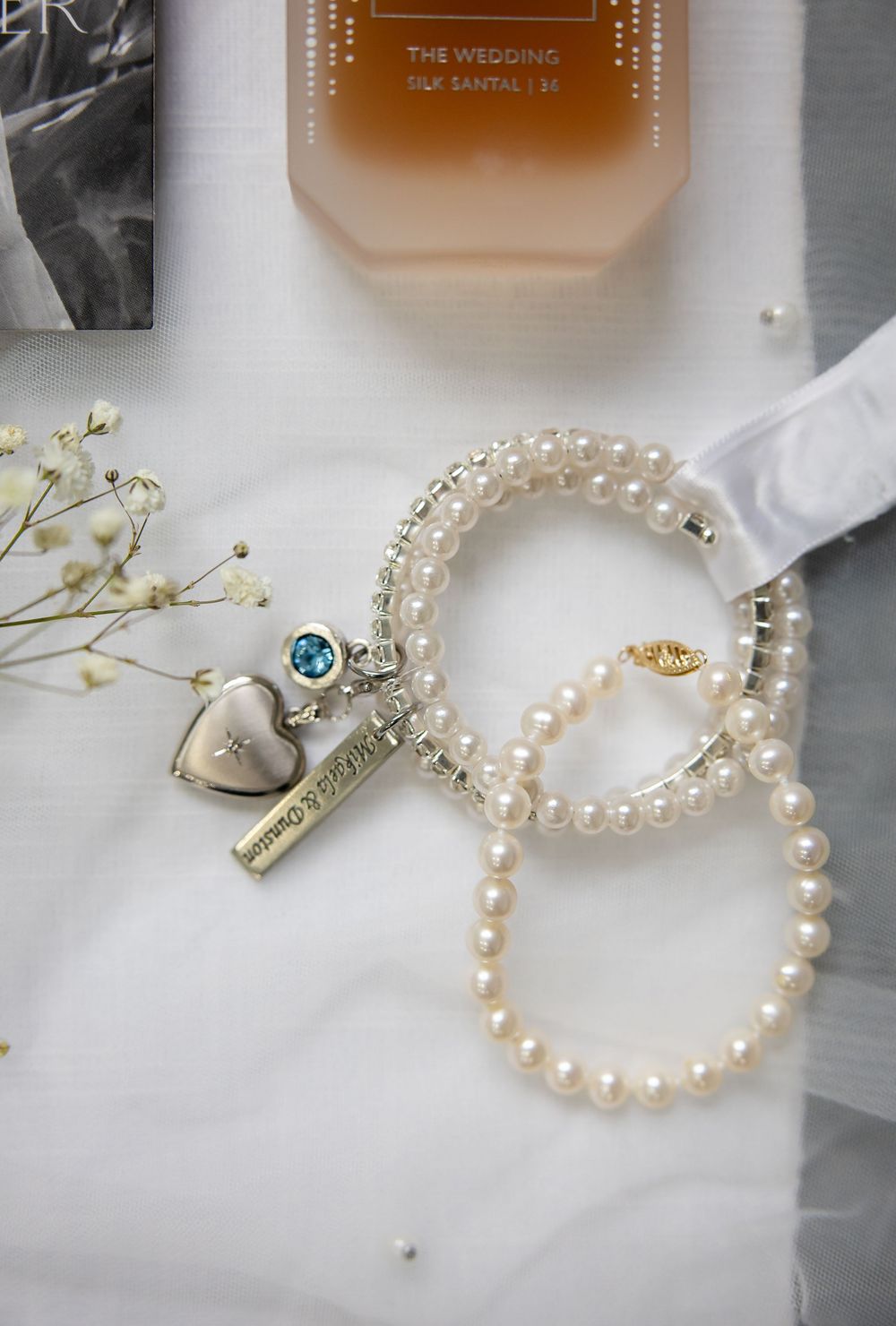 Pearl necklaces and delicate wedding accessories arranged on white fabric with small floral accents.