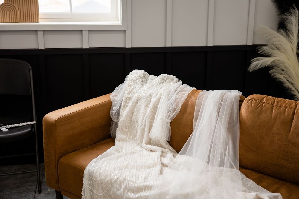 A couple in wedding attire sits intimately on a brown leather couch during their wedding photo session.