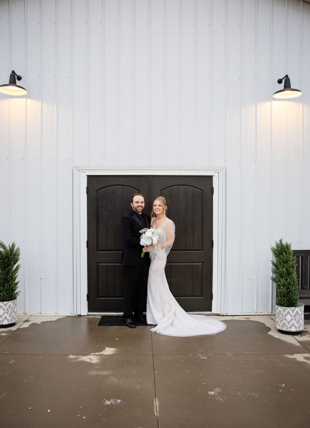 Wedding couple poses against a white barn wall with black doors in a series of romantic outdoor shots.