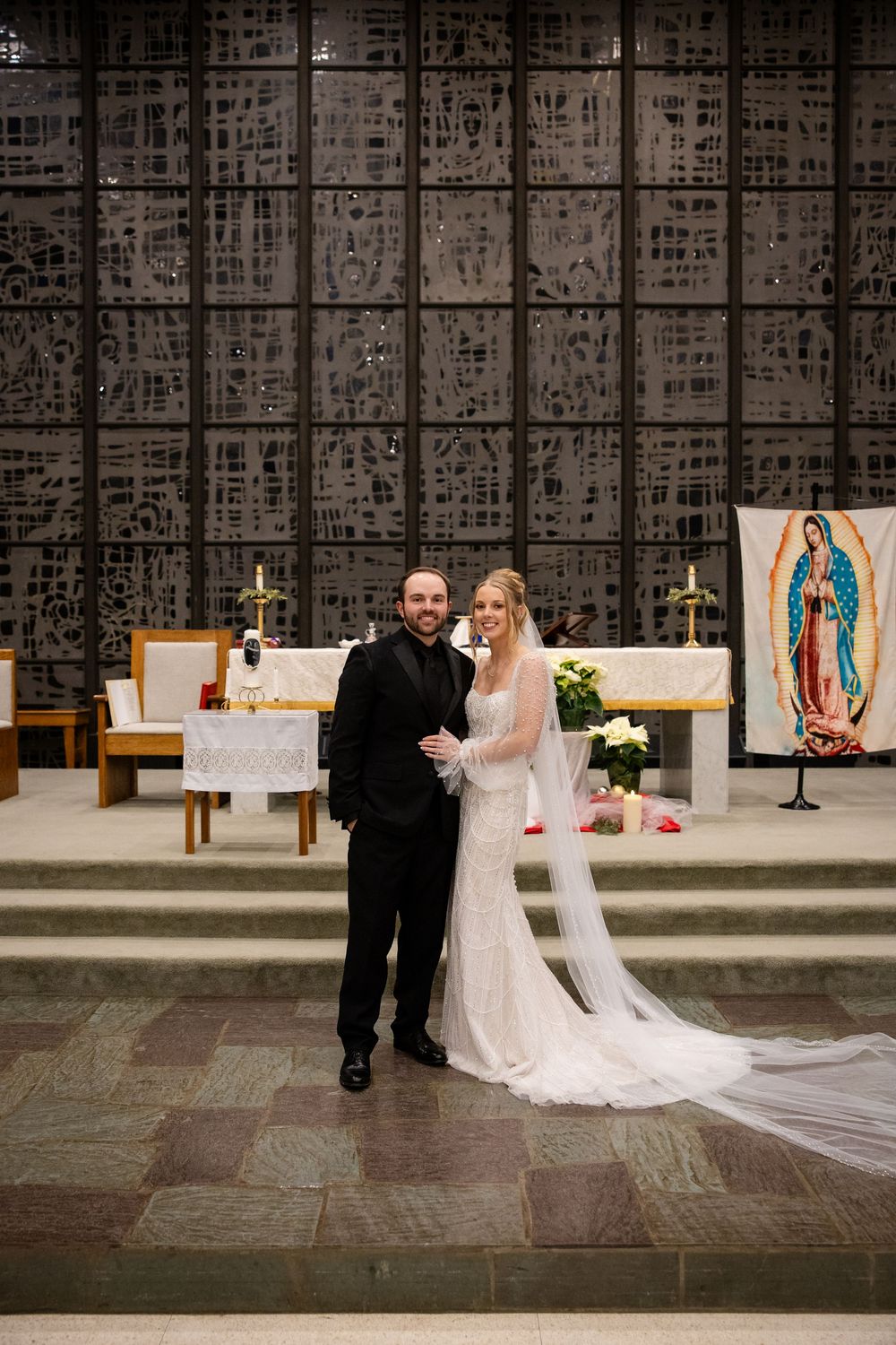 Wedding couple poses in front of a church altar with religious artwork and crosses visible in the background.