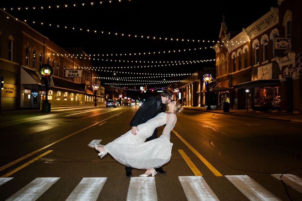 Nighttime street scene with string lights and a flowing white dress in motion on a crosswalk.
