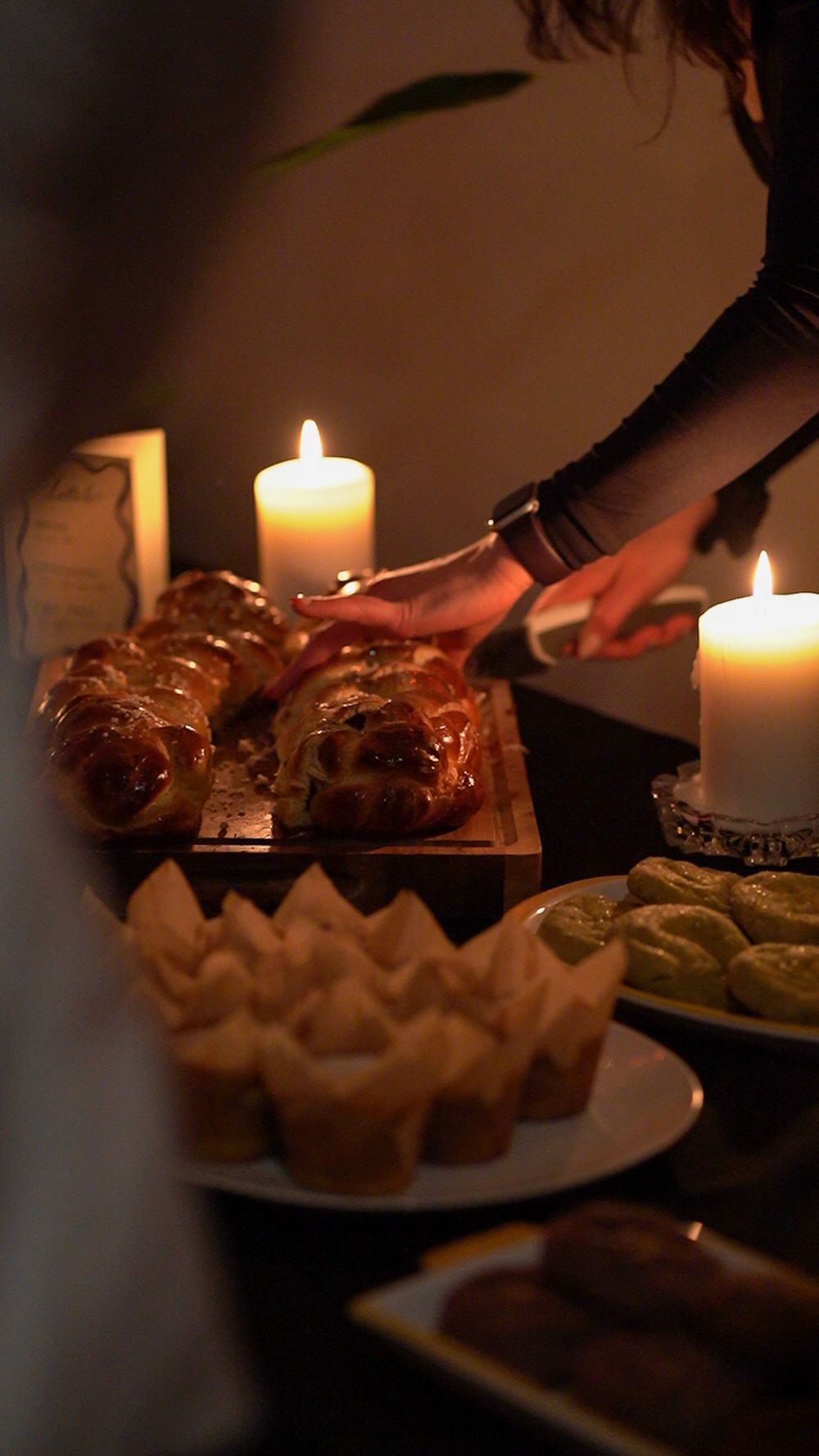 Pastries and desserts arranged on a table with glowing candles creating warm ambiance.
