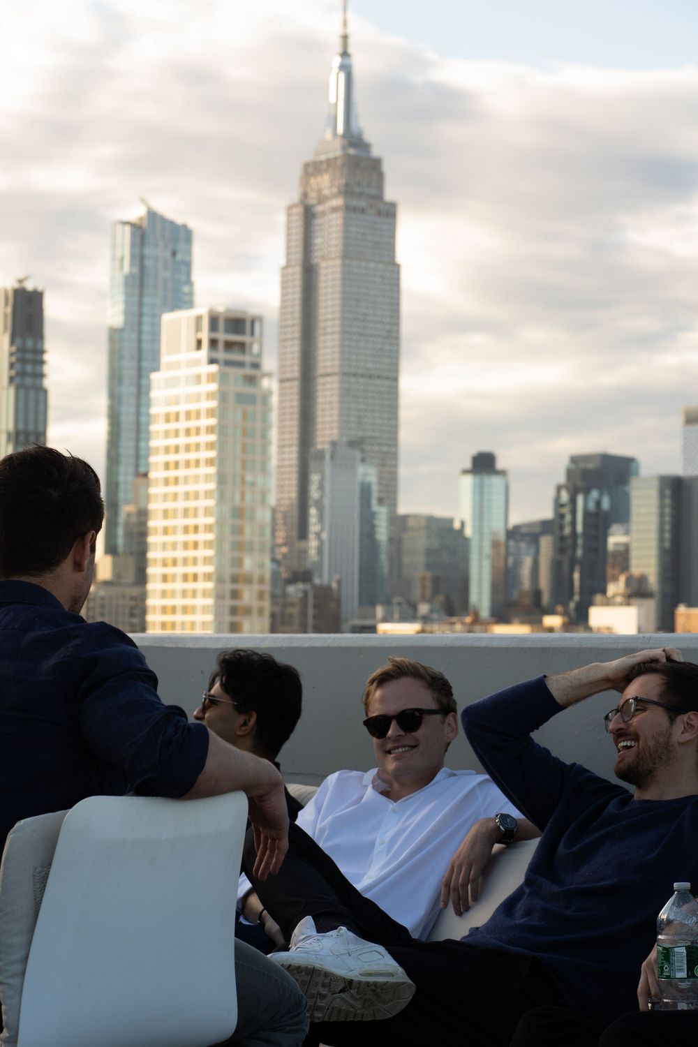Friends relaxing on a rooftop with the Empire State Building and NYC skyline in view.