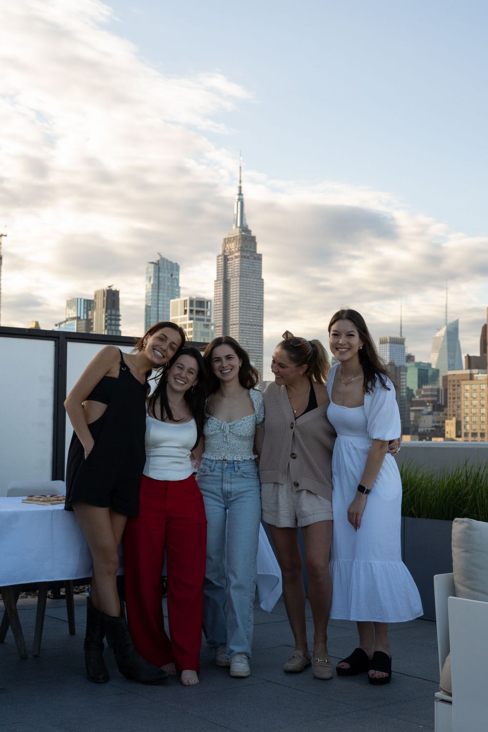 Five friends strike poses for a photo on a NYC rooftop with iconic Empire State Building in view.