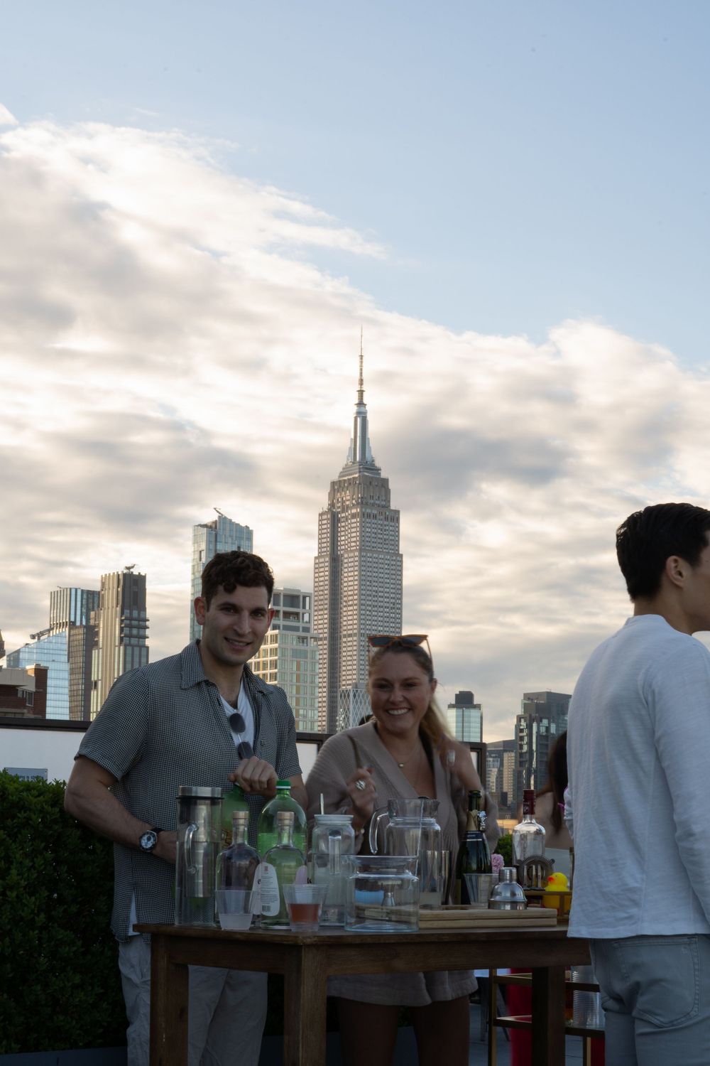 People enjoying drinks at a rooftop party with the Empire State Building and NYC skyline at dusk.