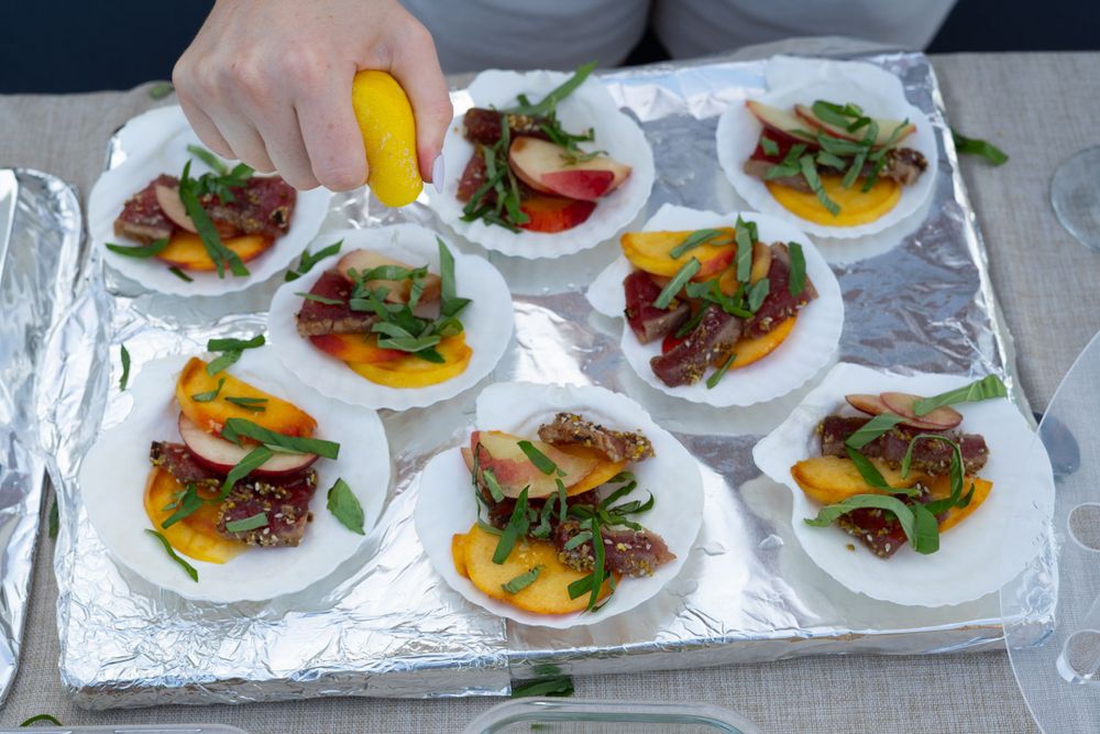 Small plates of colorful appetizers with meat and vegetables arranged on a foil-lined tray.
