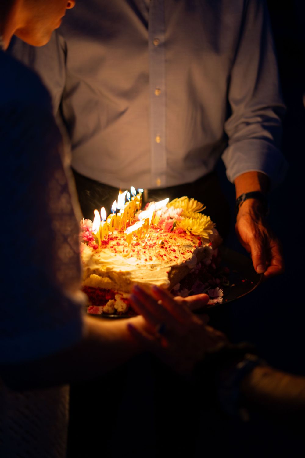 Birthday cake with glowing candles being presented in dimly lit celebration.
