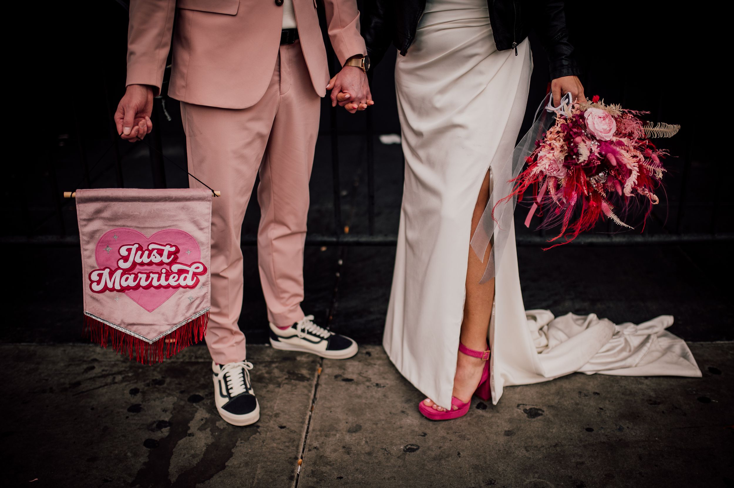 A close-up view of wedding attire showing pink and white shoes with elegant dress details against a dark background.