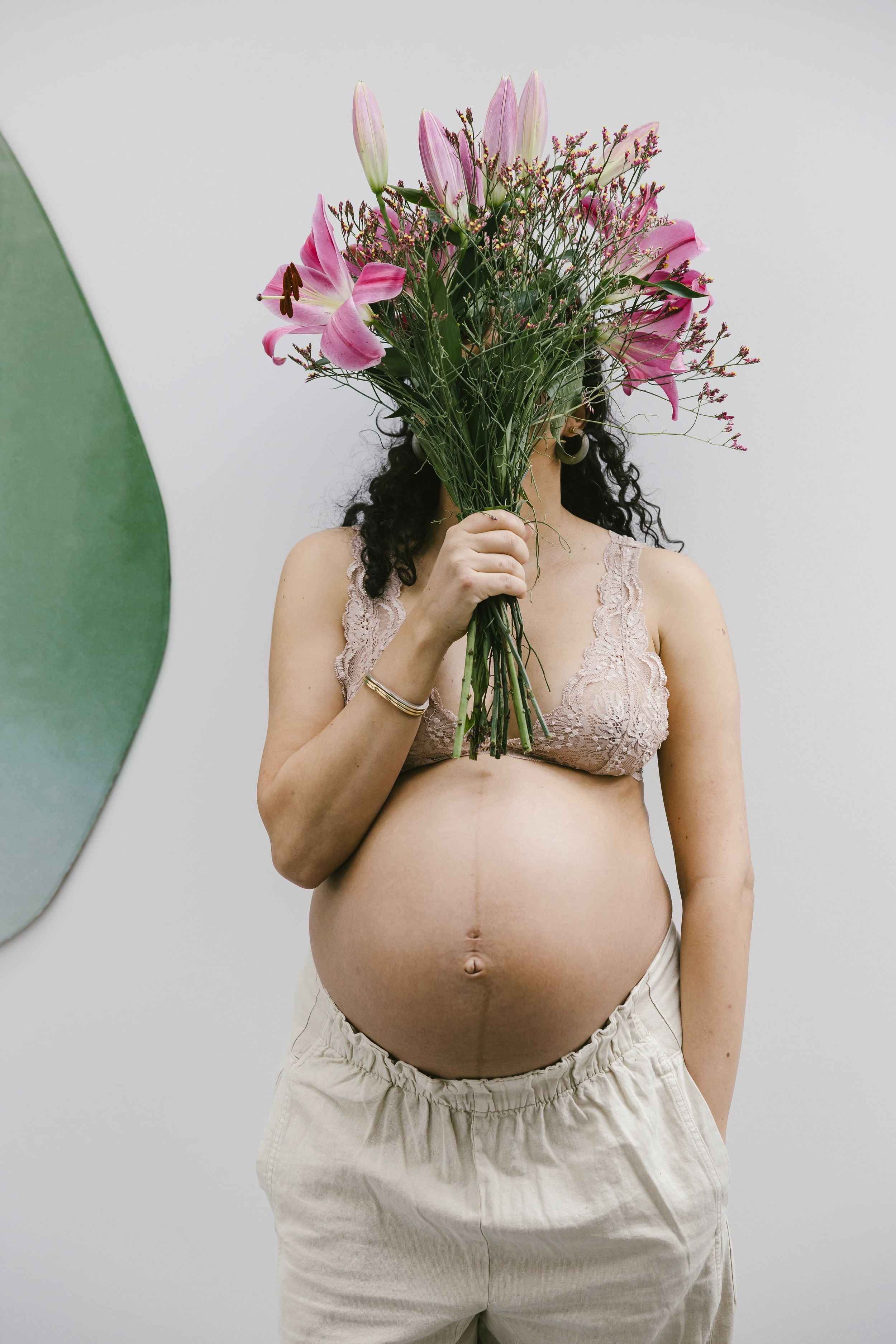 A series of maternity photos showing a pregnant belly with pink flowers held against a light background.