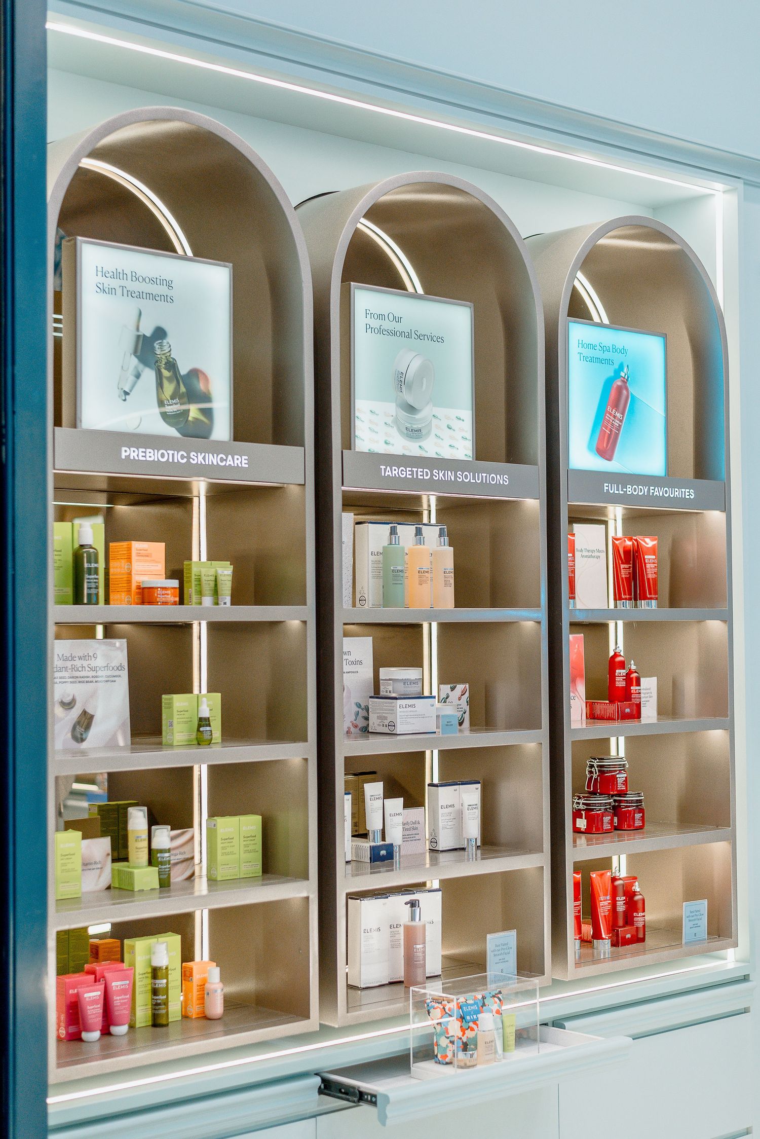 Beauty products and skincare items displayed in elegant arched shelving units with soft blue-tinted lighting.