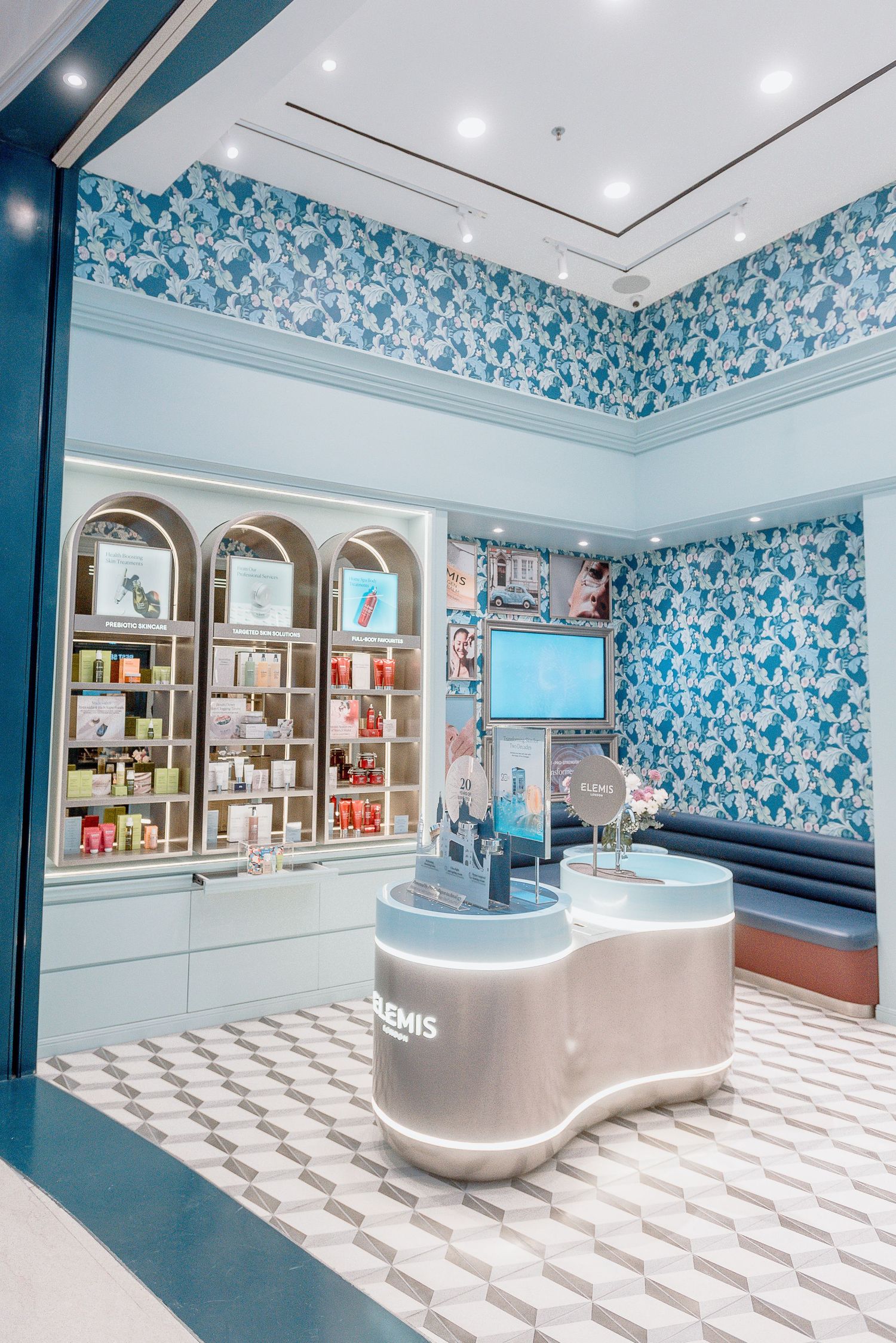 Modern spa interior with blue floral wallpaper, white curved counters, and checkered flooring in a retail setting.