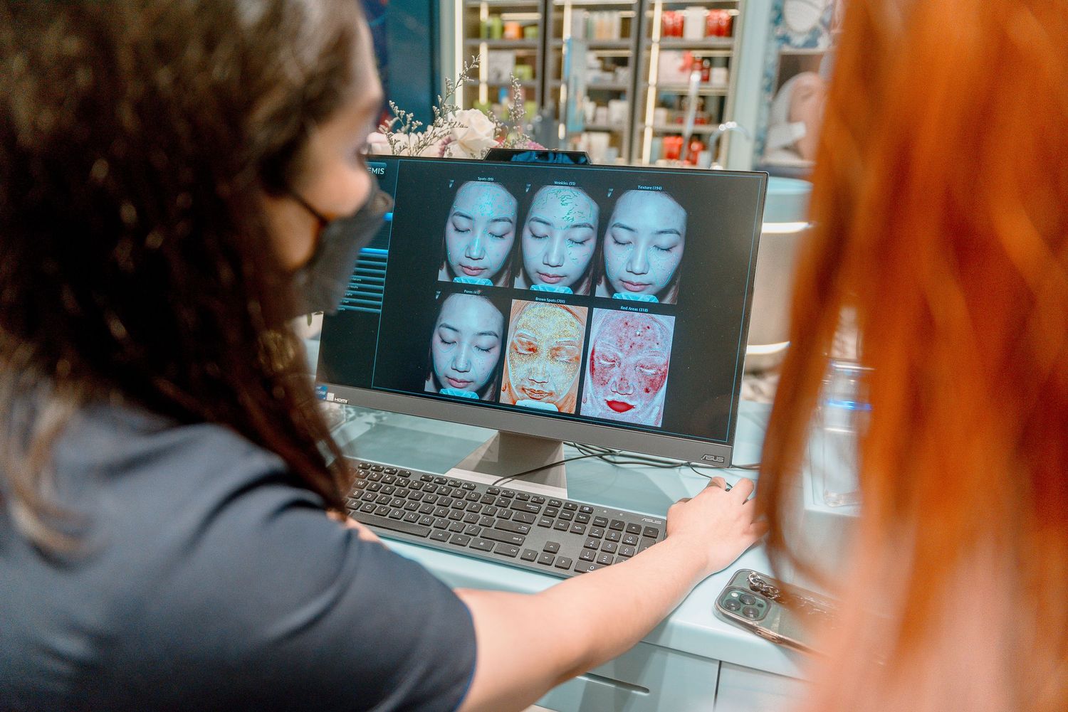 A person works on a laptop in a retail environment with shelves of products visible in the background.