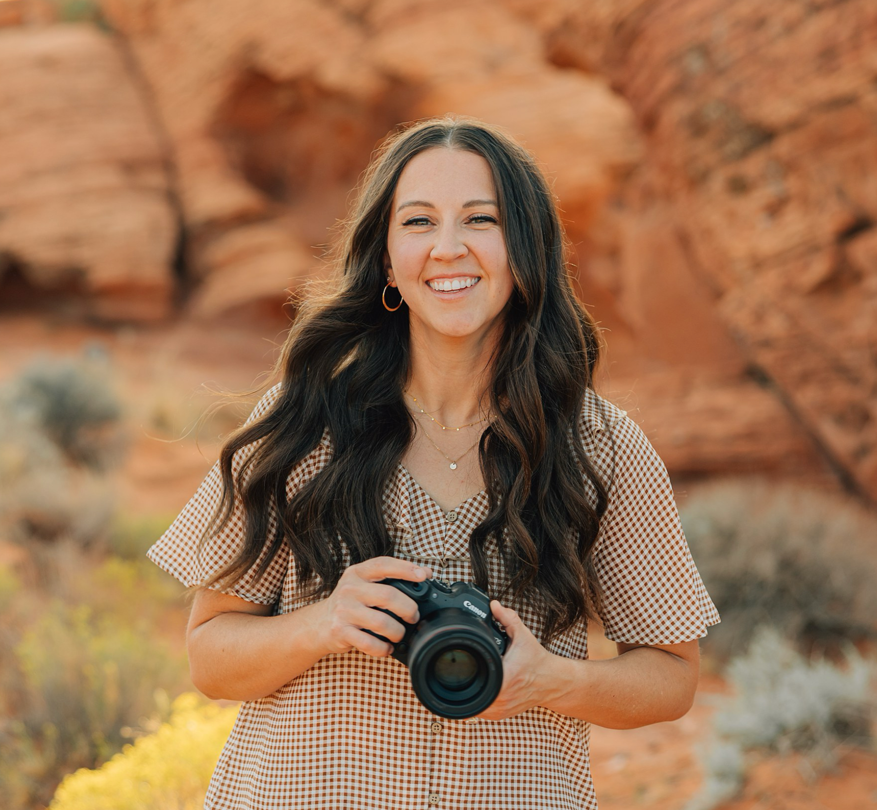 A person in a light beige dress with flutter sleeves poses against red rock formations in a desert landscape.