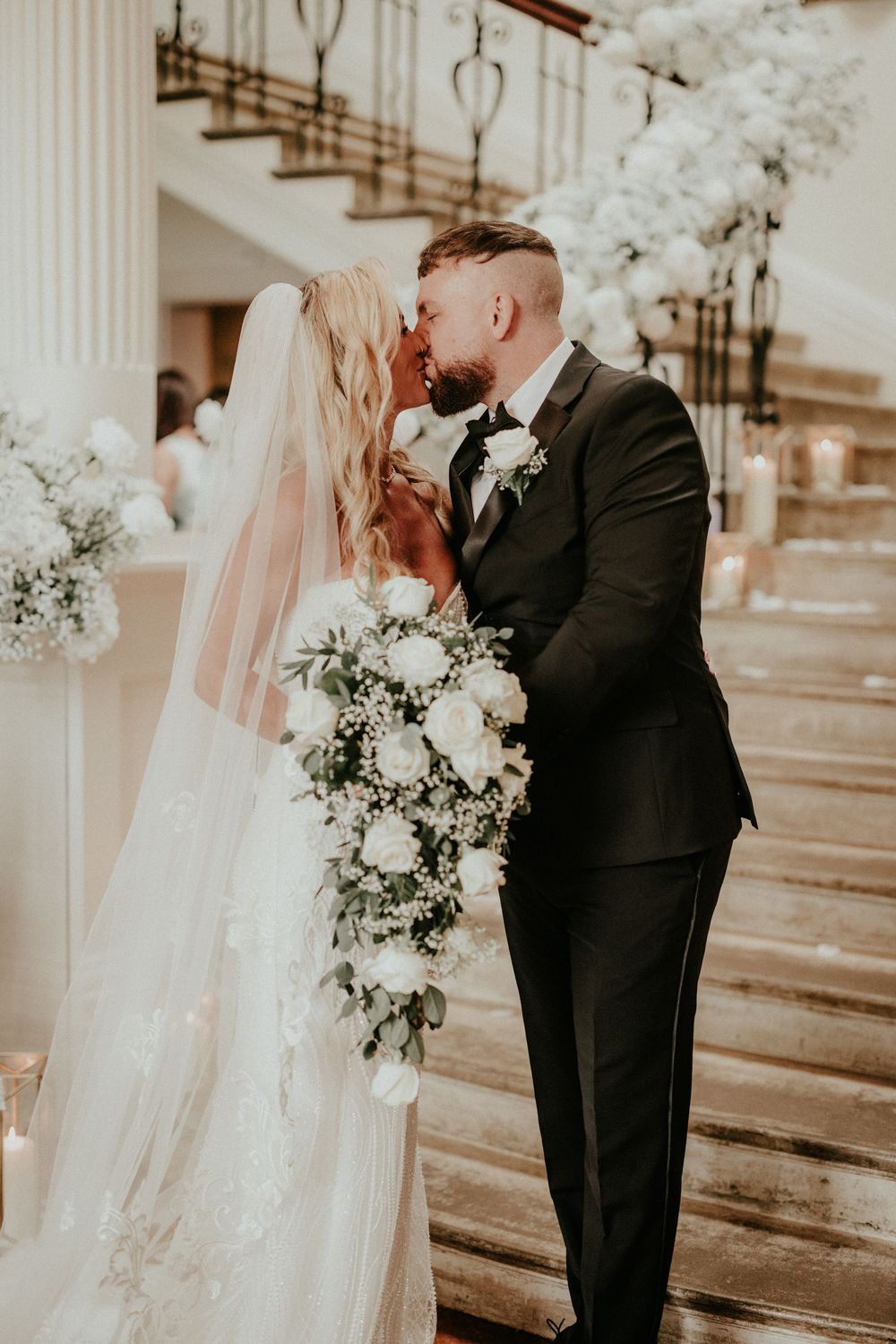 Romantic wedding couple sharing a tender kiss in a church with white floral decorations and natural light.