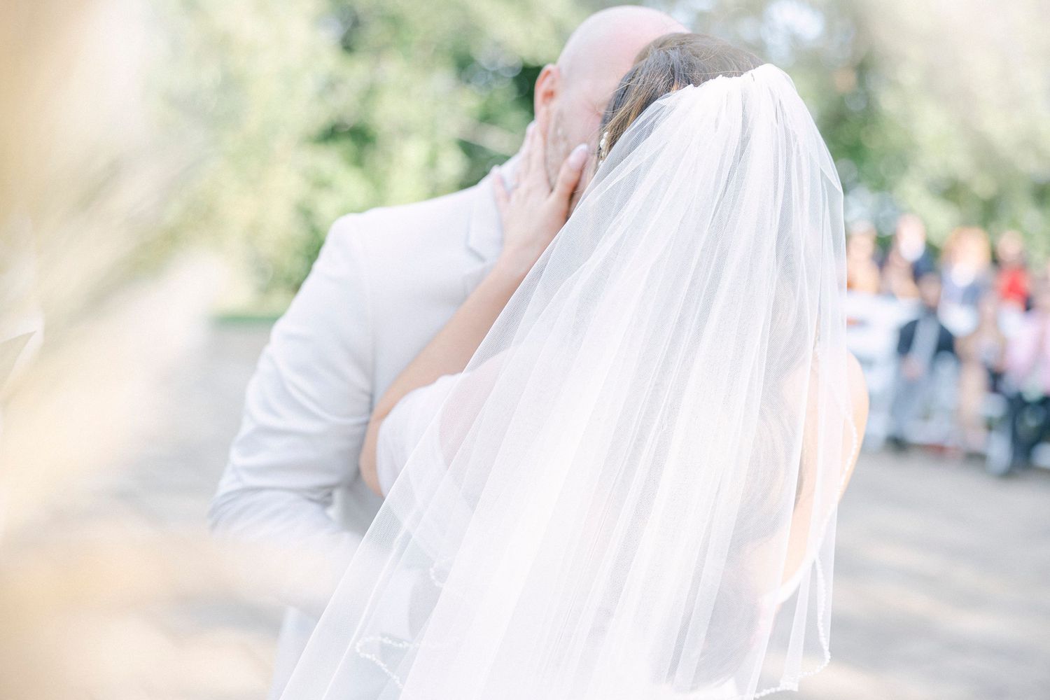 Bride and groom sharing a tender kiss during outdoor wedding ceremony, bride wearing flowing white veil.