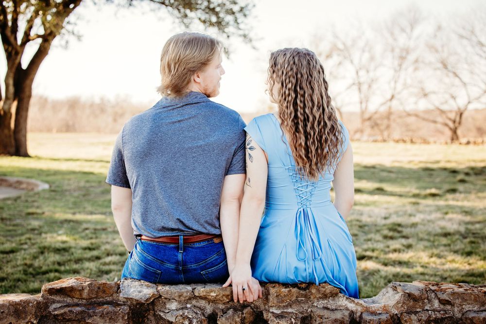 Couple in blue outfits sitting together on a grassy hill during golden hour sunset.