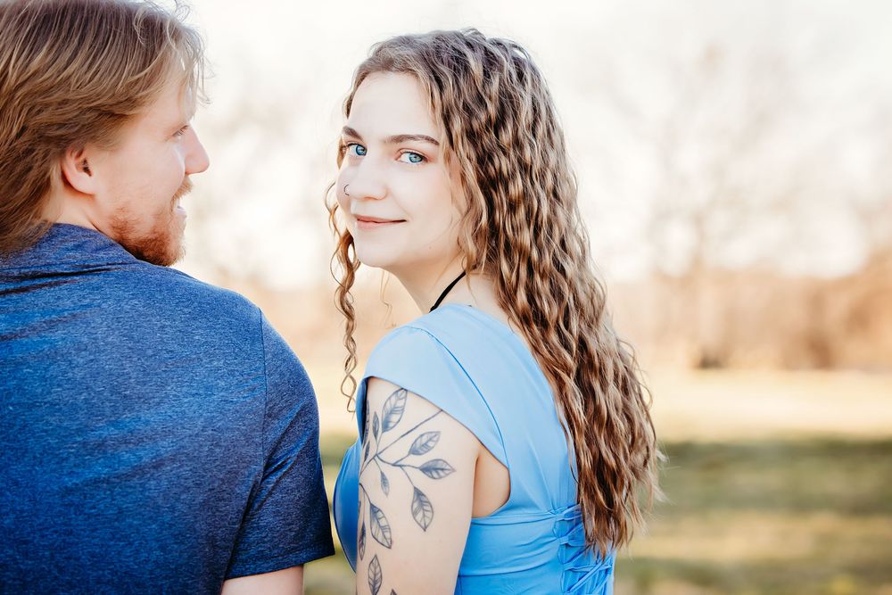 A romantic engagement photo session in a park shows a couple in blue outfits sharing tender moments together.