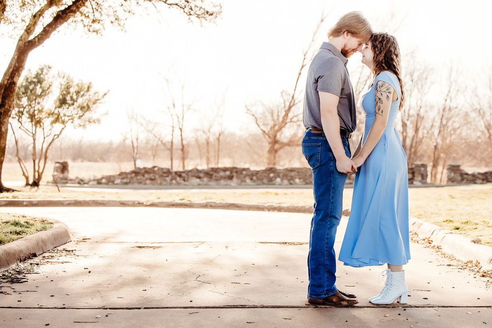 A couple in blue outfits poses with their husky dogs in a natural outdoor setting at sunset.