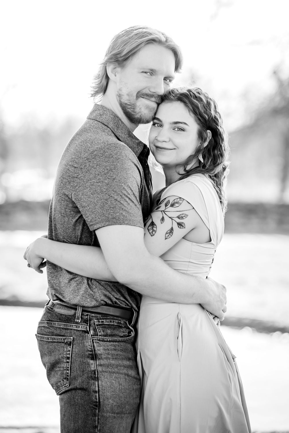 A romantic black and white portrait of a couple embracing outdoors in casual attire.