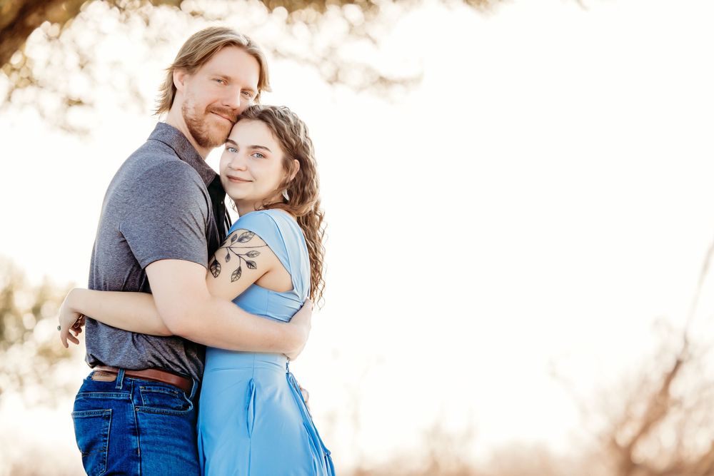 Romantic outdoor portrait of couple embracing in blue clothing against sunlit natural backdrop.