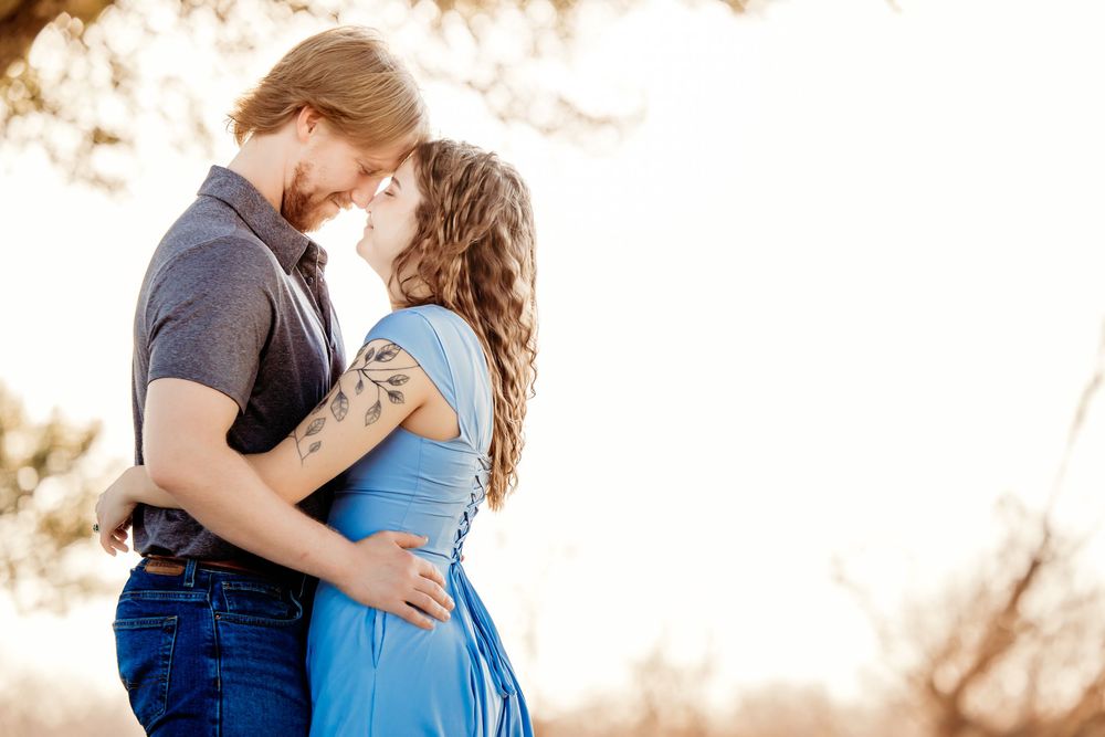 Couple shares tender moment outdoors as sunlight filters through trees creating dreamy atmosphere.