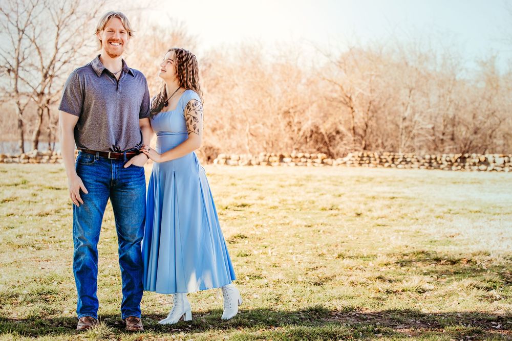 A couple shares a romantic moment in a sunlit field wearing coordinating blue and denim outfits.