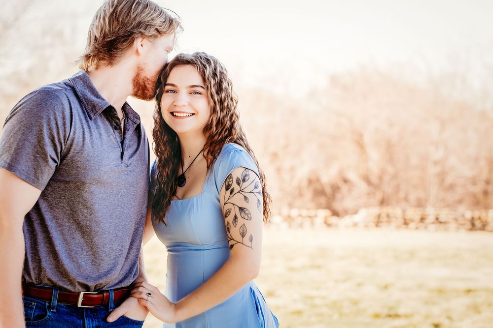 A romantic couple embraces in a sun-drenched field during golden hour with mountains in the background.