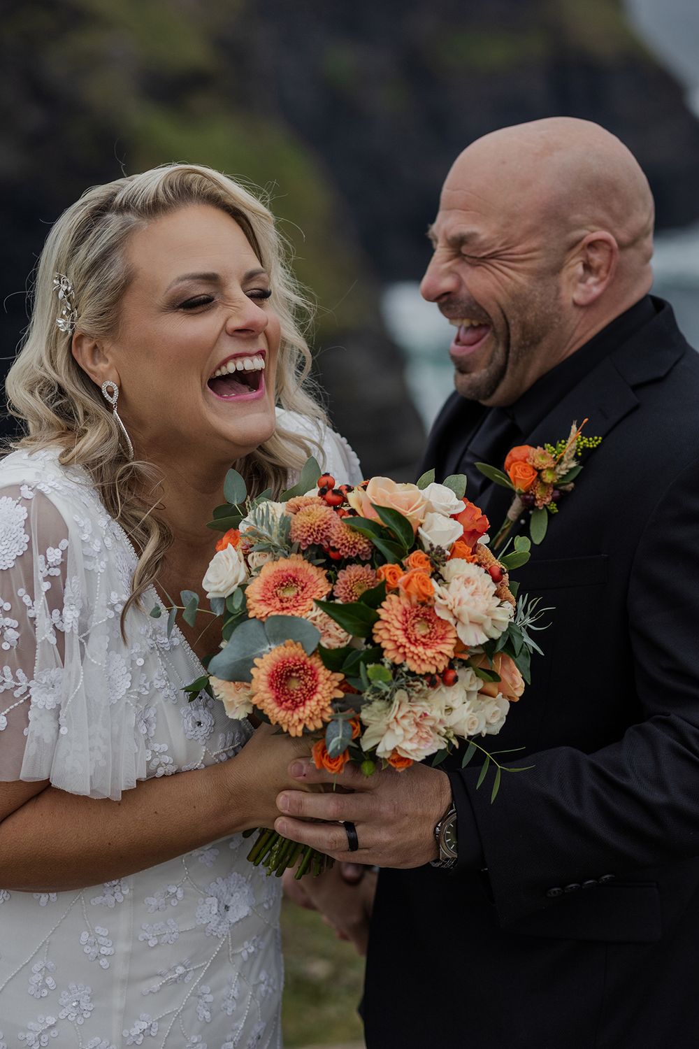Bride and groom laughing in the Irish wind during cliffside session.