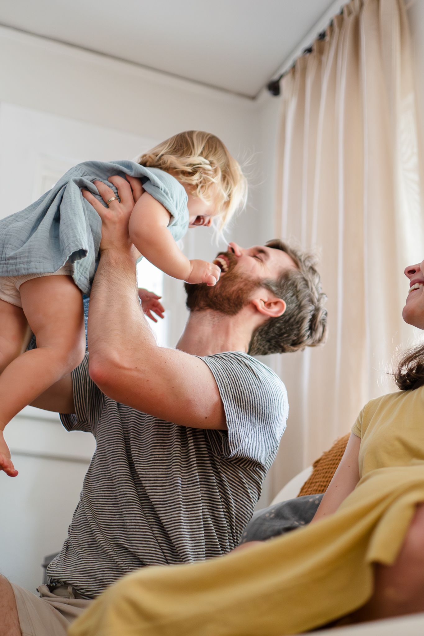 A parent and child play together on a couch, lifting the child up in a playful moment in their living room.