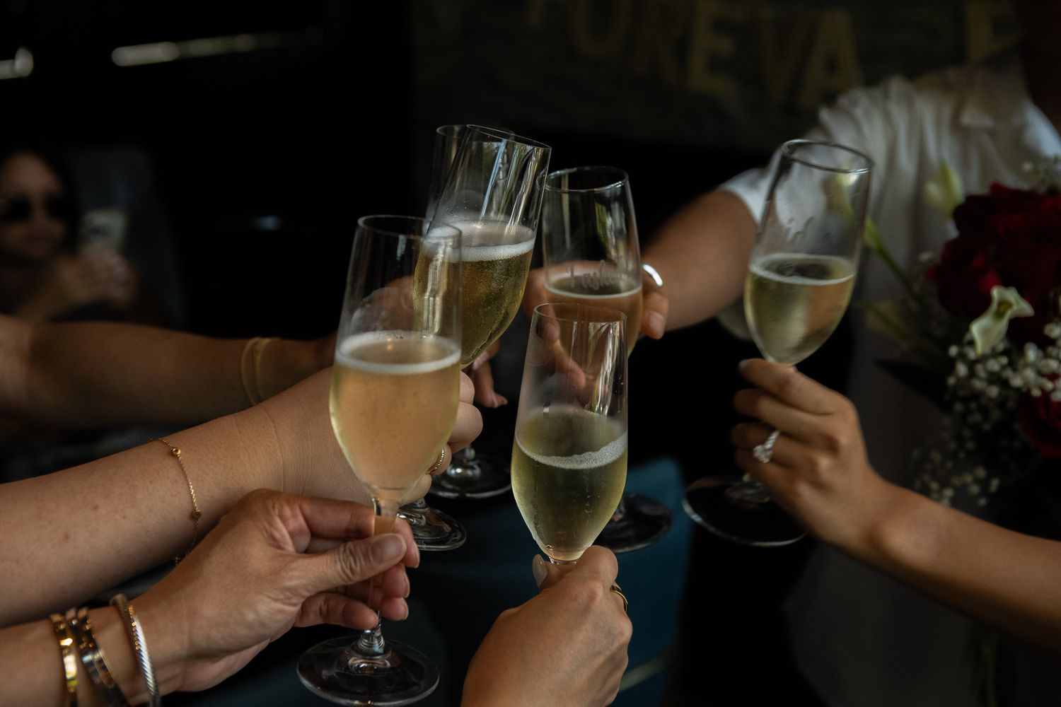 Hands holding champagne glasses in a celebratory toast against a dark background.