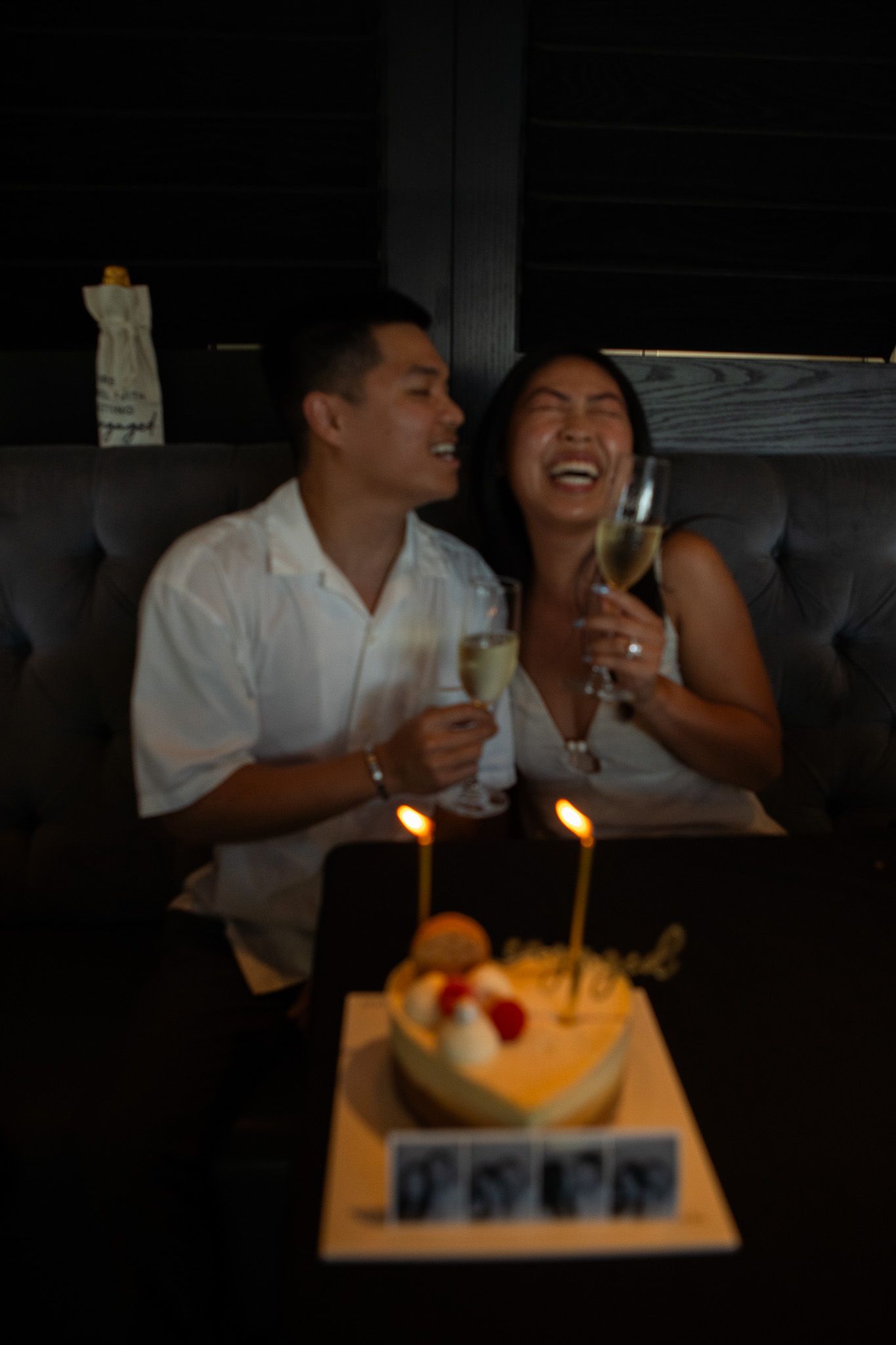 A couple sharing drinks and laughter at a candlelit table with dessert.