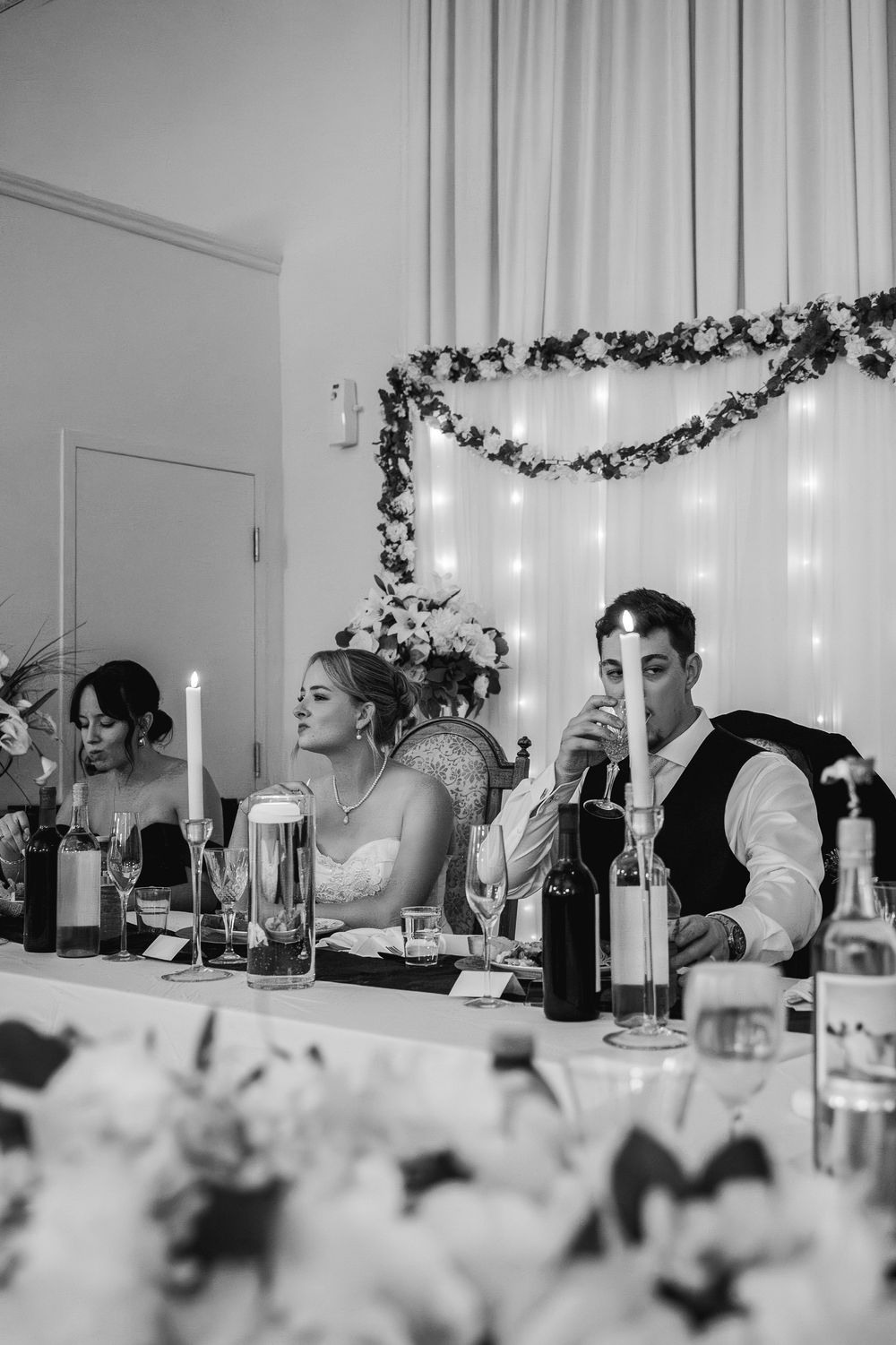 Black and white panoramic photo of wedding guests seated at a long table during reception dinner.