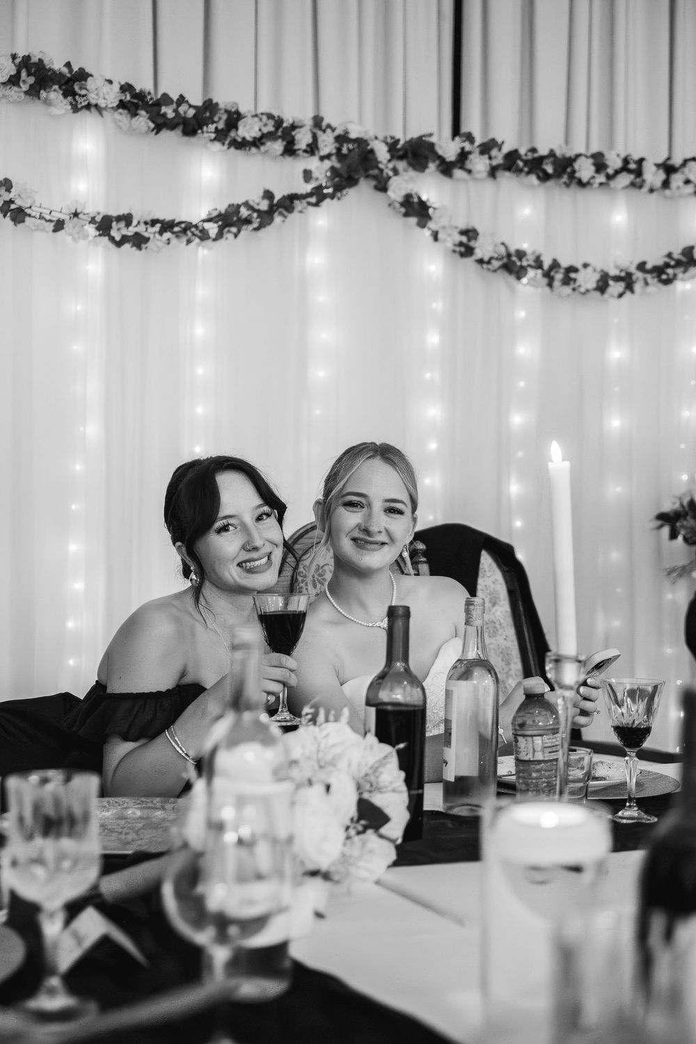 Wedding reception guests enjoy drinks and conversation at a table decorated with string lights and garland.