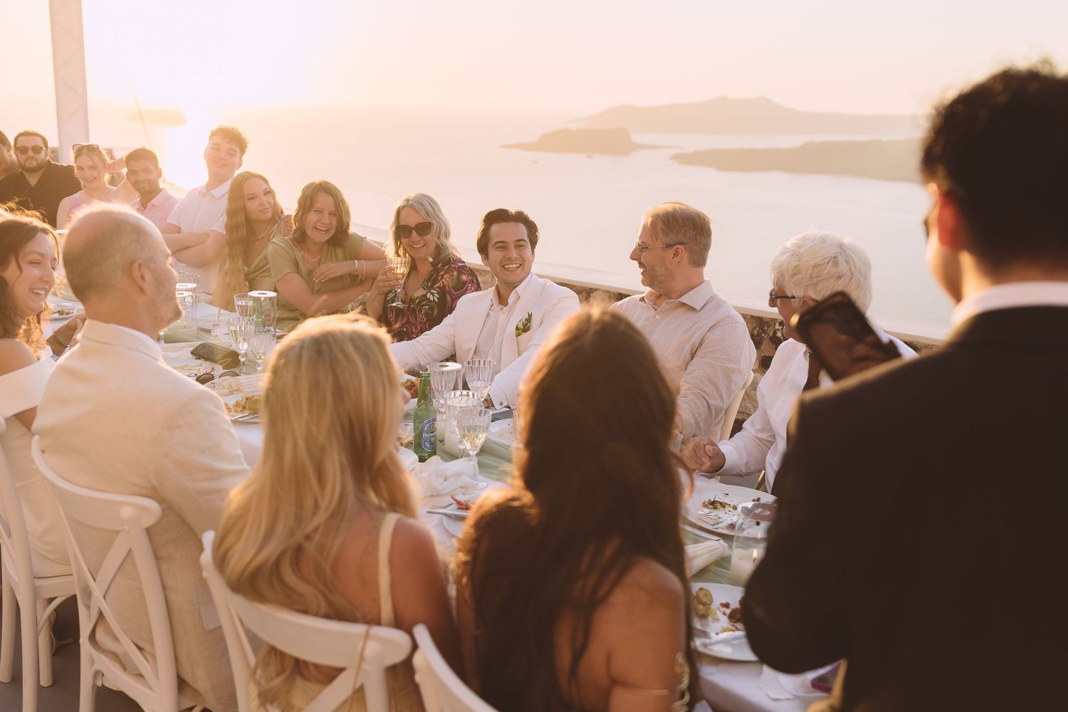Guests listening to speeches at a Santorini destination wedding. at sunset with caldera views behind them.