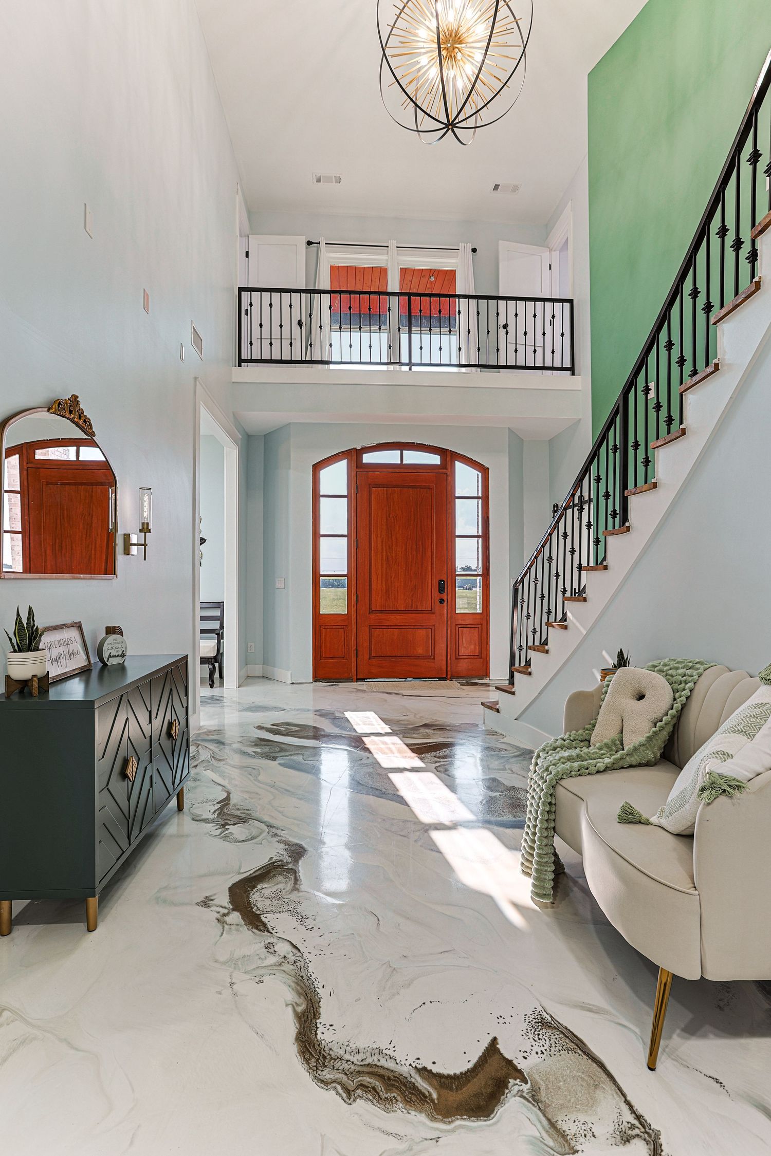 Modern white foyer with marble floors, wooden front door, green staircase railing, and elegant chandelier lighting.