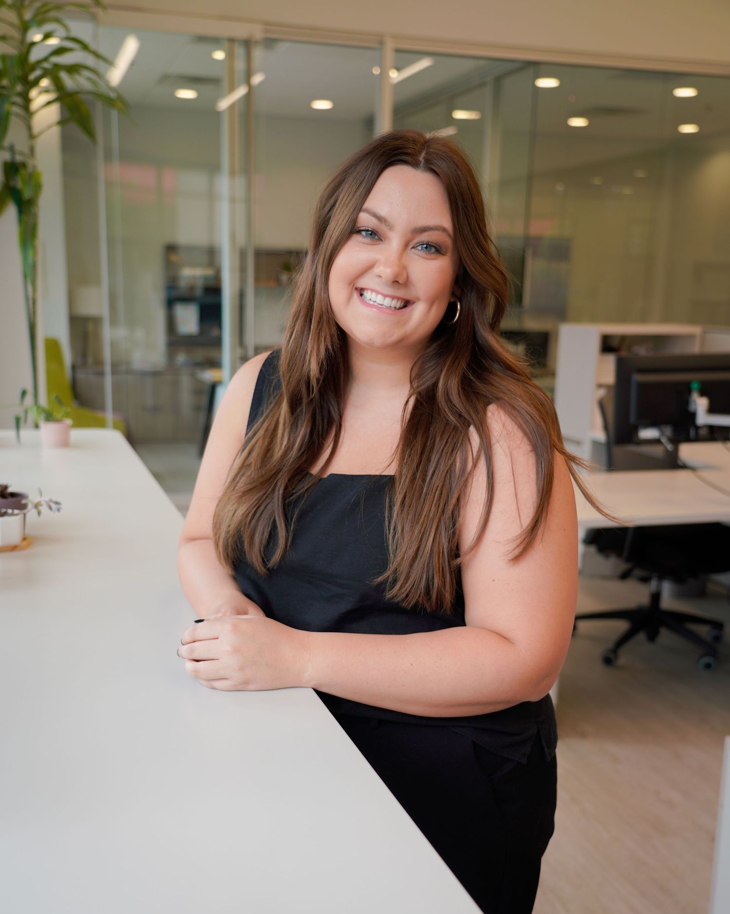 Professional business portrait of someone in a black sleeveless top smiling warmly in a modern office setting.