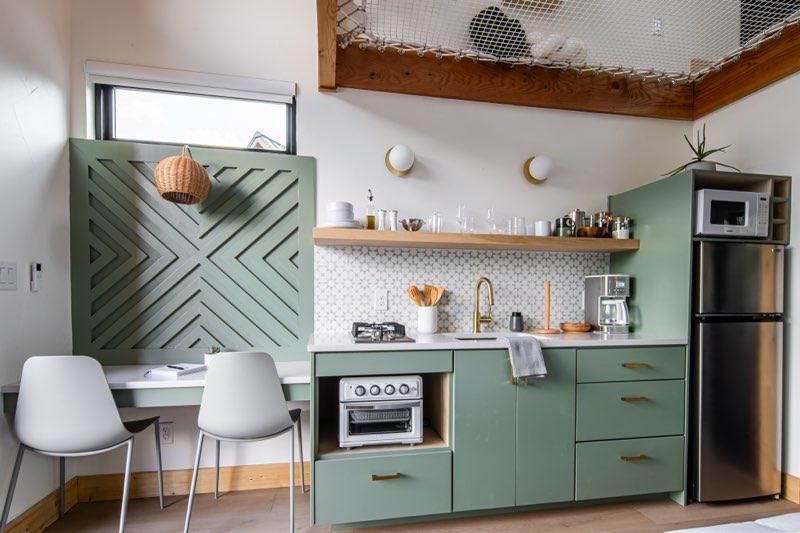 Modern kitchen features sage green cabinets with chevron wall pattern and brass hardware accents.